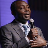 African pastor in gray suit talking into microphone